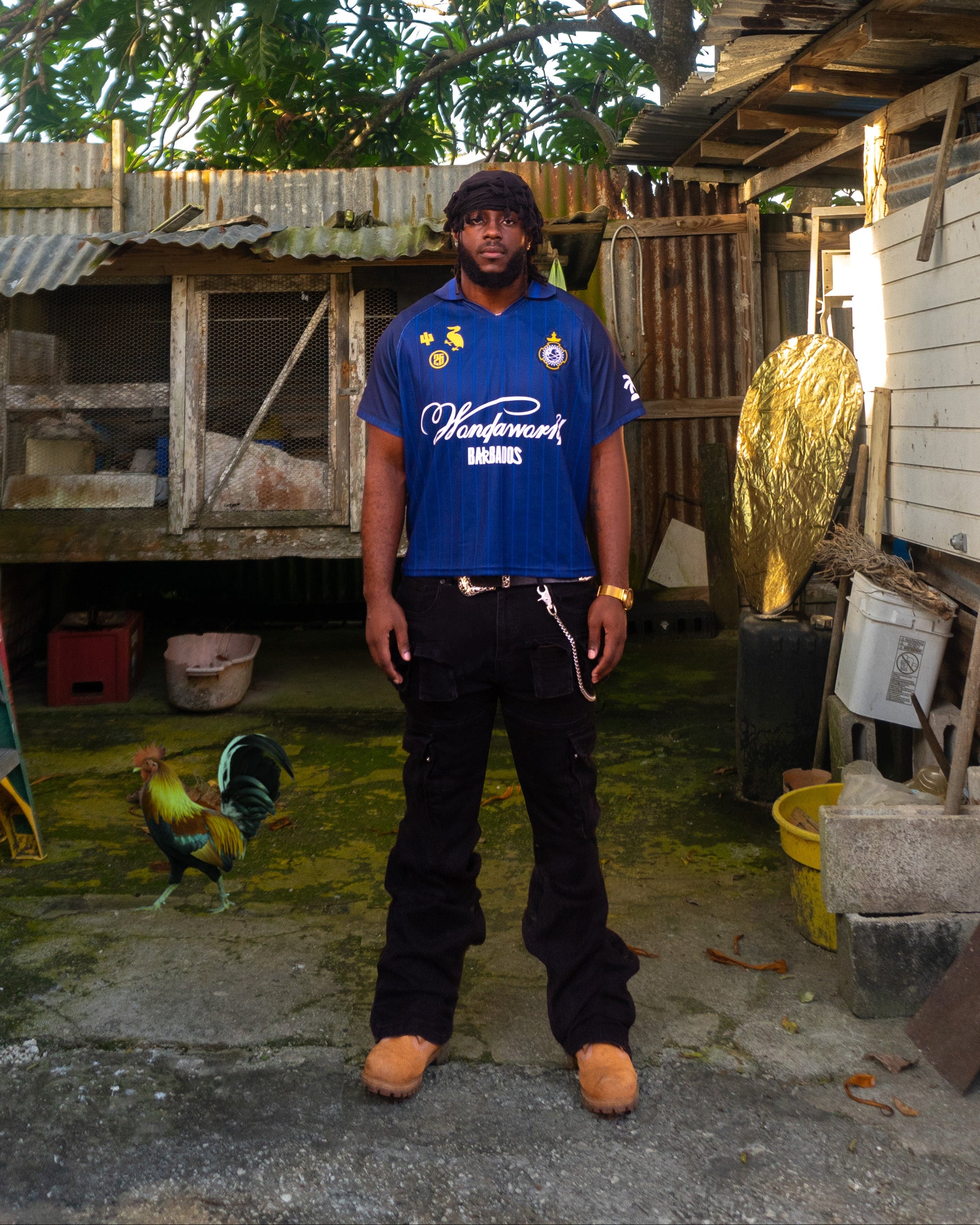 Person wearing a blue shirt standing in front of a wooden structure with trees in the background